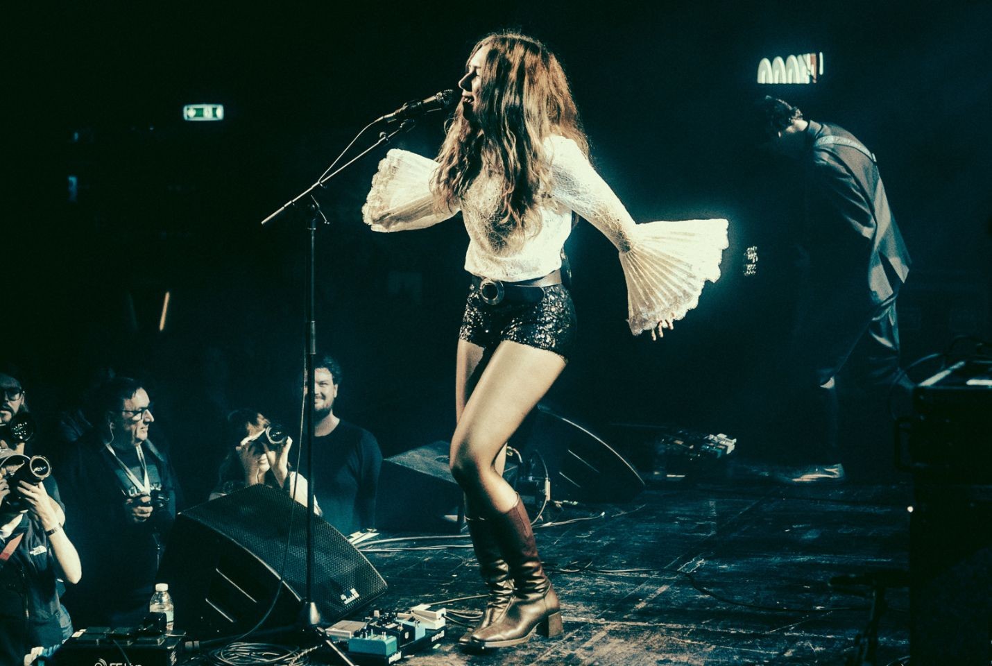A woman performing on stage wearing black sequinned shorts and a white bell sleeve lace top